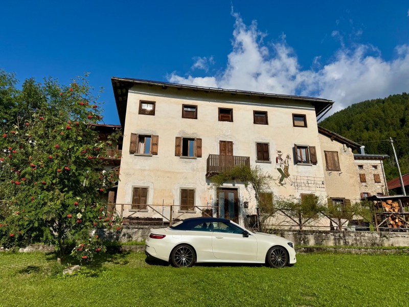 Dolomites in summer - big white house with car parked outside in Pozzale for a fraction of the price of a small room in Cortina