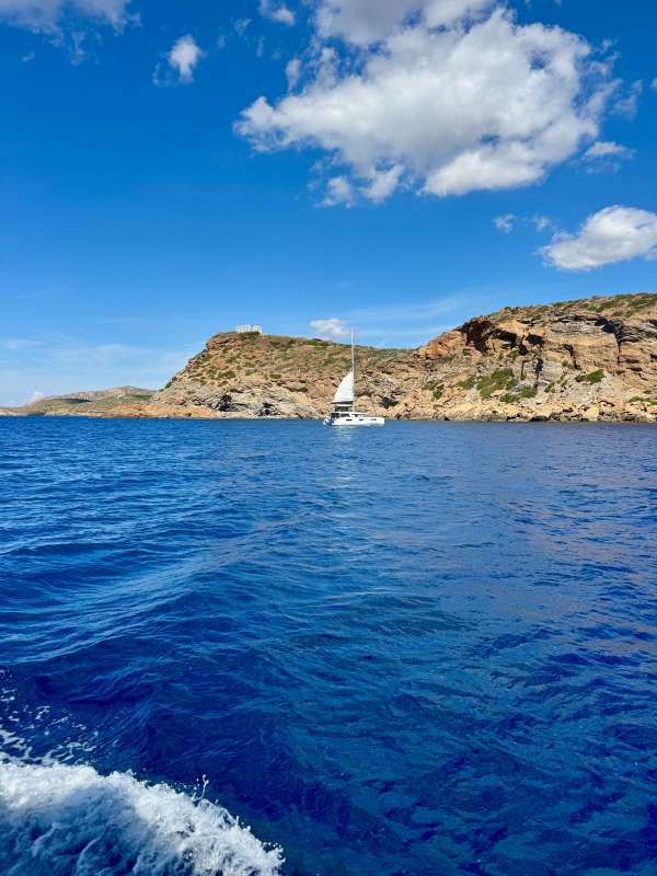 Sailing yacht off a rocky Cyclades island, viewed from the water.